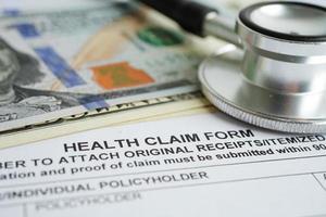 Health claim form with stethoscope and US dollar banknotes, insurance accident medical concept. photo