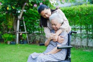 Caregiver help Asian elderly woman disability patient sitting on wheelchair in park, medical concept. photo