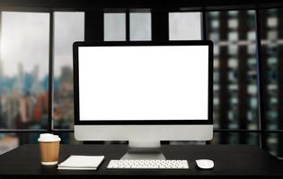 computadora del espacio de trabajo puesta en un escritorio de trabajo de madera y rodeada de una taza de café, un portapapeles, una planta en maceta, una pila de teléfonos inteligentes, tabletas y teclados ordenados en la oficina foto