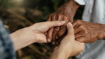 Hands of the old man and a woman hand on the wood table in sun light photo