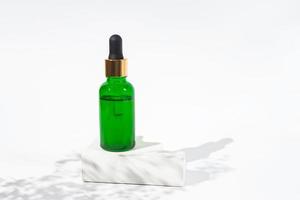 Green bottle with cannabis oil used for medical purposes. White background with daylight and flowers shadows. Soothing cbd oil. Alternative Medicine photo