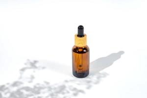 Amber dropper bottle with serum or gel on white background with daylight with beautiful flowers shadows. Skincare natural cosmetic. photo