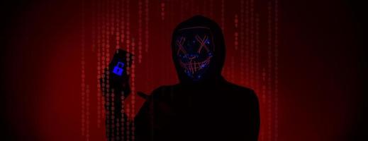 Digital security Concept. Anonymous hacker with mask holding smartphone hacked. photo