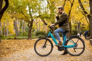 Joven con bicicleta eléctrica en el parque de otoño foto