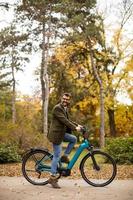 Joven con bicicleta eléctrica en el parque de otoño foto