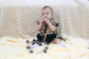 Cute little baby girl in beautiful green dress is playing with Christmas lights on soft plaid. Home vibes at Christmas time or Birthday. photo