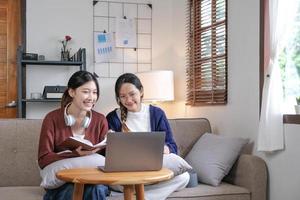 dos estudiantes asiáticos aprendiendo juntos en línea con una computadora portátil y un tutor juntos en casa. foto