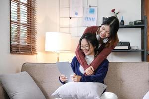 Beautiful Asian lesbian couple hugging their boyfriend in the living room. Two attractive female friends sit on the sofa watching movies on a tablet in the living room. feel happy and enjoy photo