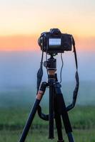 black digital camera on tripod shooting foggy morning landscape at summer with selective focus photo