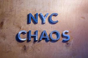 las palabras nyc chaos colocadas con letras de metal sobre una superficie plana de madera contrachapada bajo luces policiales blancas y azules. concepto. foto