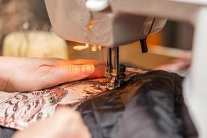 una vista de cerca del proceso de costura, la mano de una anciana usando una máquina de coser, técnica de enfoque selectivo foto