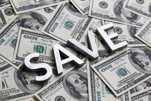 The word SAVE laid with white metal letters on the americal dollar banknotes background with selective focus photo
