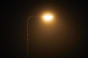 One night lamppost shines with faint mysterious yellow light through evening fog, copy space photo