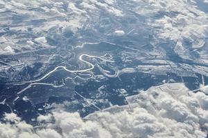 Aerial view over clouds top to snow covered rivers, fields and roads, winter fresh frosty air photo