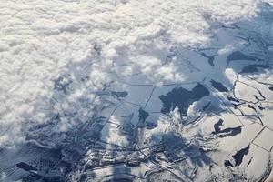 Aerial cloudscape view over clouds top to snow covered rivers, roads, cities and fields, winter air photo