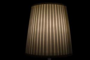 Lampshade lamp. Lamp is in dark. Light on black background. Ribbed paper. photo