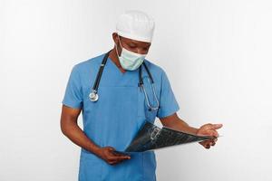 Black surgeon doctor man in blue coat white cap and surgeon mask holds x ray image, white background photo