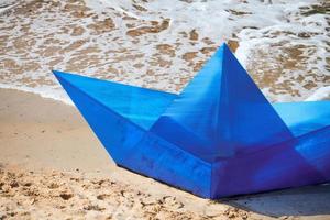 Origami blue paper boat on sandy beach for concept design, beautiful blue paper ship, close up photo