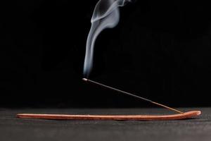 Smoke curls of burning incense stick in wooden holder for relaxation and meditation black background photo