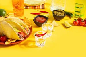 tragos de tequila mexicano con lima y chile rojo caliente con tacos de maíz de comida tradicional en el fondo foto