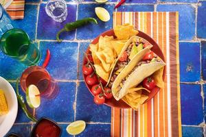 Traditional Mexican corn tacos with meat, vegetables, avocado, beans, salsa and nachos. Served with various sauces and drinks. Top view. Big family gatherings. photo