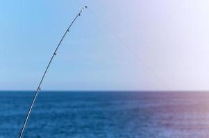 Fishing rod against blue ocean or sea background, copy space. Waiting for biggest haul. Meditative relax sport. photo