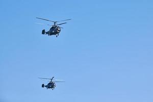 Two military helicopters flying in vibrant blue sky performing demonstration flight, air show photo
