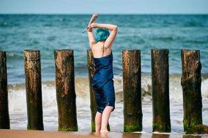 artista de actuación de mujer de pelo azul con vestido azul de pie en la playa sosteniendo un pincel, vista trasera foto