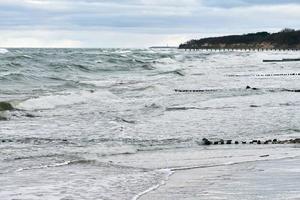 View of blue sea with foaming waves and wooden breakwaters photo