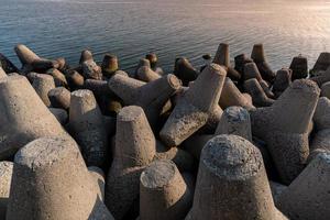 Tetrapod breakwaters in sea water. Beautiful sunset seascape with concrete tetrapodes for protect coastal structures from storm sea waves, effects of weather and longshore drift photo