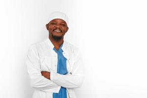 Smiling black surgeon doctor bearded man in white coat and cap with crossed arms isolated on white photo