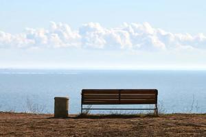 Empty bench with trashcan on cliff before sea background, peaceful quiet place for thinking alone photo