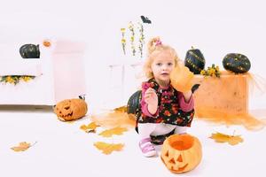 funny and cute little blonde curve girl with pumpkin in Halloween decoration photo