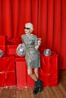Senior stylish elegant woman with glass of sparkling wine on red background. Party, fashion, celebration, anti age concept photo