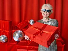 mujer elegante senior con regalos sobre fondo rojo. fiesta, moda, celebración, concepto anti edad. foto