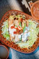 Mexican flautas with lettuce, avocado, cream, sauce and fresh water photo