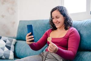 mujer feliz comprando en su celular con una moneda bitcoin en la mano foto