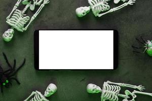 Four skeletons are lying near the smartphone on a dark background. photo