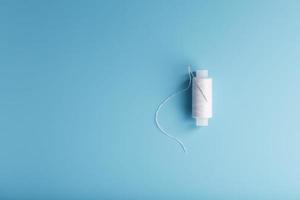 A spool of white thread with a needle on a blue background. photo