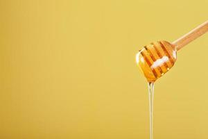 Golden honey trickles from a wooden honey dipper on a yellow background photo