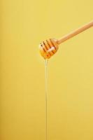 Natural Honey flows down from a honey bucket on a yellow background. photo