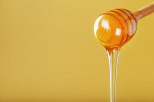 Honey drips in a thin stream from a honey dipper on a yellow background. photo