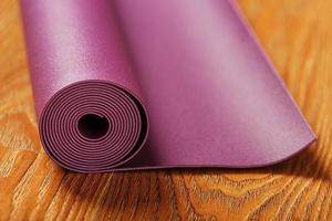 An unfolded lilac-colored yoga mat is unfolded on the wooden floor. photo