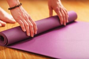 una niña coloca una alfombra de yoga lila antes de una práctica de entrenamiento en casa en un piso de madera. foto