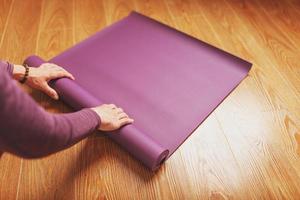 A man lays out a lilac yoga mat on the wooden floor of a house photo