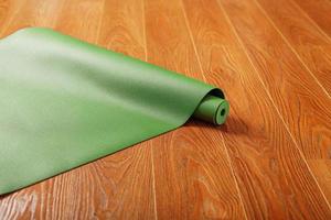 A green yoga mat is laid out in a roll on the wooden floor. photo