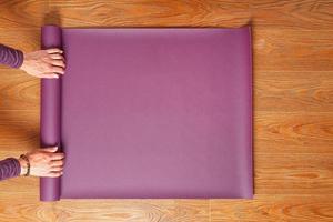 A woman's hands fold a lilac yoga or fitness mat after a workout at home in the living room. photo