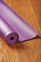 A lilac yoga mat is twisted on the wooden floor. photo