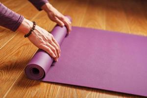 las manos de una mujer doblan una alfombra lila de yoga o fitness después de un entrenamiento en casa en la sala de estar. foto