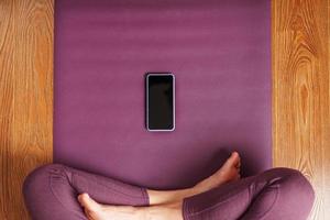 una chica practicando yoga y meditación en casa sobre una alfombra lila usando un smartphone y una aplicación móvil. foto